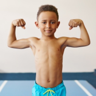Children, fitness, health and ethnicity concept. Portrait of dark skinned black boy of school age exercising at gym, preparing for competition, posing topless, demonstrating his tensed muscles